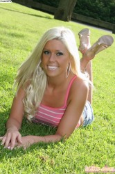 Сексуальная блондинка в джинсовых шортиках лежит на траве