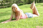 Сексуальная блондинка в джинсовых шортиках лежит на траве